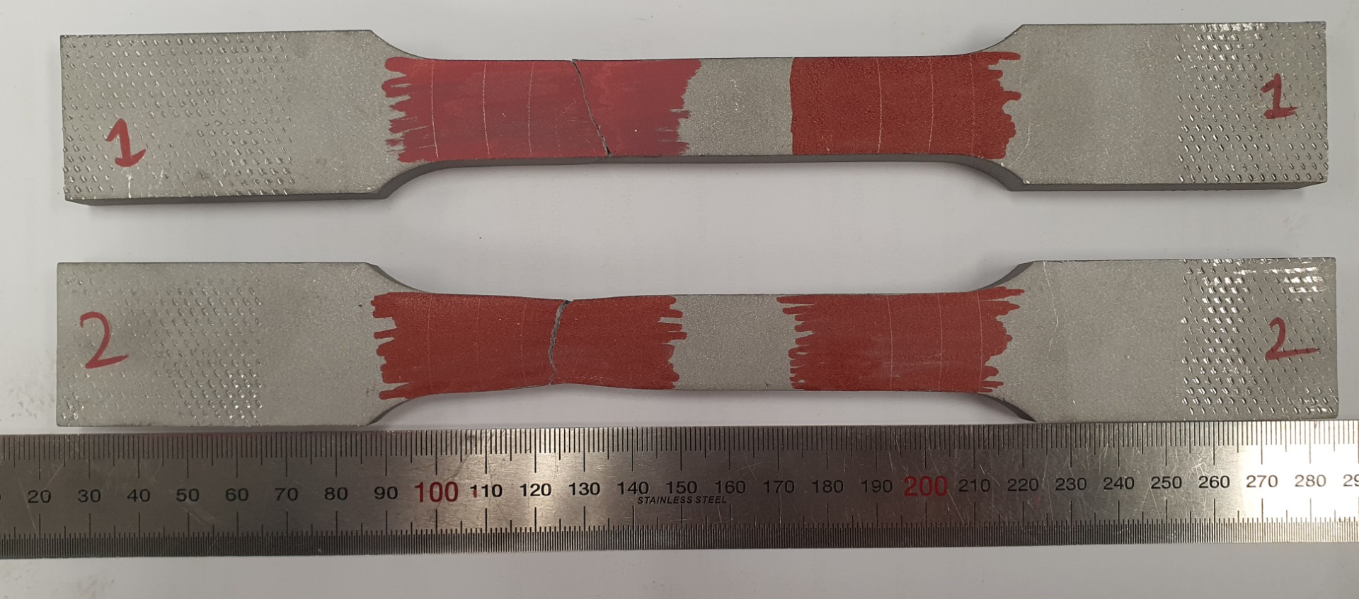 Fractured tensile specimens after testing to UTS, with red marker applied